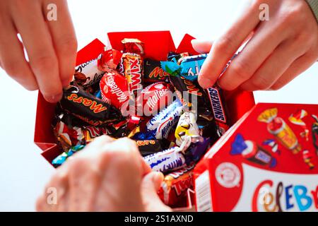 Nahaufnahme der Hände auf einer Party, die Schokolade aus der Schachtel mit Mini-Pralinen nimmt: SNICKERS, MARS, TWIX, BOUNTY, GALAXY, MALTESERS Teasers, Stockfoto