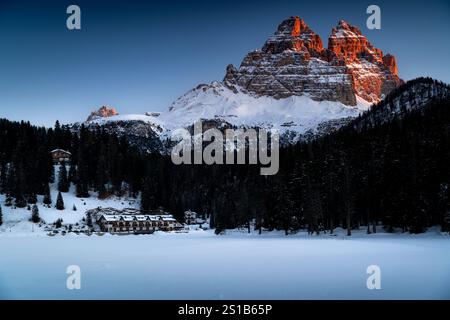 Blick auf die schneebedeckten Gipfel des Tre Cime di Lavaredo vom Misurina-See in den ersten Sonnenstrahlen. Gefrorener See und scharfe Berggipfel in den Alpen. Stockfoto
