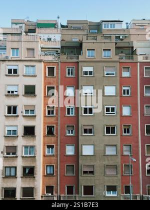 Fassade eines mehrstöckigen Wohngebäudes in Beige-, Orange- und Rottönen, mit Fenstern und Balkonen unter klarem blauen Himmel Stockfoto