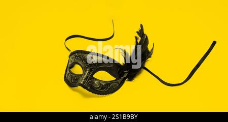 Venezianische Karnevalsmaske mit schwarzer Federdekoration isoliert auf Gelb Stockfoto