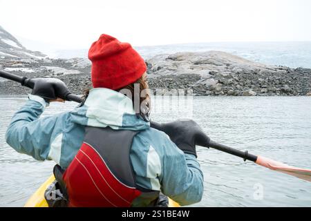 Eine junge brünette Frau in ihren 30ern von hinten gesehen, wie sie auf einem Gletschersee in Norwegen mit einem Kajak in Richtung des riesigen Jostedal-Gletschers mit extremer Natur paddelt Stockfoto