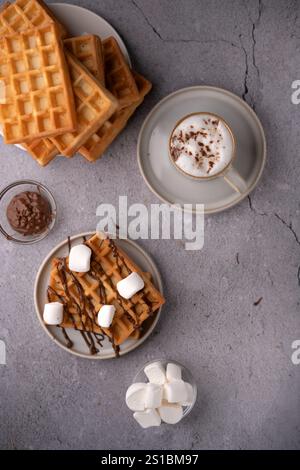 Köstliche hausgemachte Waffeln mit geschmolzener Schokolade und flauschigen Marshmallows serviert zusammen mit einer cremigen Tasse heißem Kakao auf einer rustikalen Steinplatte Stockfoto