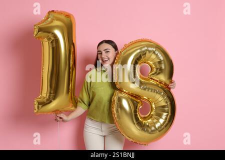 Coming of Age Party - 18. Geburtstag. Glückliche junge Frau mit zahlenförmigen Ballons auf rosa Hintergrund Stockfoto