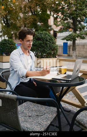 Mann, der draußen in einer entspannten Umgebung an Laptop und Notizen arbeitet Stockfoto