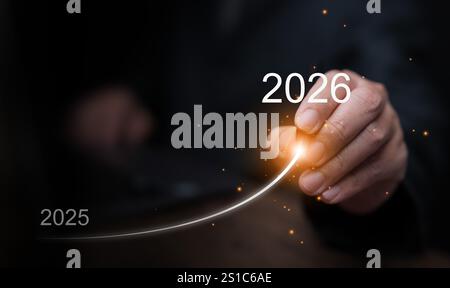 Frohes neues Jahr. Ein Geschäftsmann zieht eine Linie, die von 2025 bis 2026 aufsteigt und für zielgerichtetes Wachstum, Leistung und Erfolg steht, um den zu starten und zu begrüßen Stockfoto