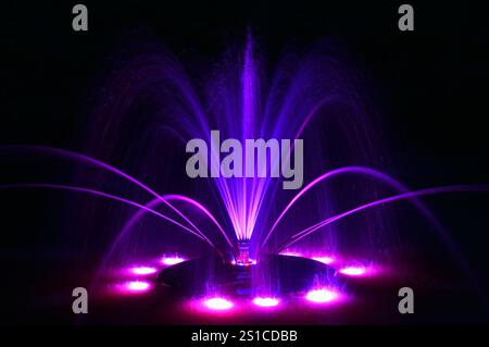 Schwimmender Springbrunnen in Neonviolett Blau, große detaillierte, farbige horizontale Nahaufnahme bei Nacht, beleuchtete, leuchtende Farbe wechselnde helle Lichter des Stadtparks Stockfoto