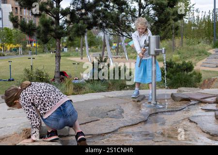 Zwei Schwestern, 8 und 7, spielen mit einem Wasserspiel auf einem Spielplatz in Brent Cross Town, einem Bauprojekt in NW London Stockfoto