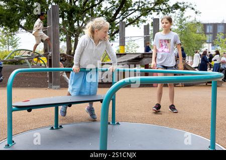 Ein siebenjähriges weißes Mädchen dreht sich auf einem Kreisverkehr auf einem Spielplatz in Brent Cross Town, einem Bauprojekt in NW London. Ihre 8-jährige Schwester ist hinter ihr. Stockfoto