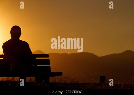 Ein Mann sitzt auf einer Bank und beobachtet den Sonnenuntergang vom Oyamada Ryokuchi Park, Machida, Tokio, Japan. Stockfoto