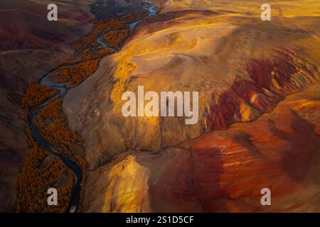 Aus der Vogelperspektive sehen Sie einzigartige rote und orangene Berge mit einem sich windenden Fluss, der atemberaubende Erosionsmuster in einer marsähnlichen Landschaft zeigt. Aufnahme in einer abgelegenen Region des Altai-Gebirges, Russland. Stockfoto