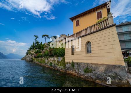 Elegante Villa am Wasser mit pastellfarbenen Wänden und Bogenfenstern, die sich entlang einer felsigen Küste mit üppigen Gärten und malerischem Seeblick unter A erhebt Stockfoto