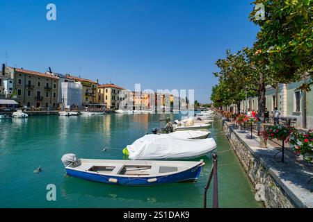 Malerische Kanalszene in einer europäischen Stadt mit farbenfrohen Gebäuden, vertäuten Booten und einer von Bäumen gesäumten Promenade mit leuchtenden Blumen. Ruhiges Wasser Stockfoto