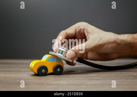 Eine Hand hält ein Stethoskop an einem Spielzeugauto. Fahrzeugwartung oder Fahrzeugdiagnosekonzept. Stockfoto
