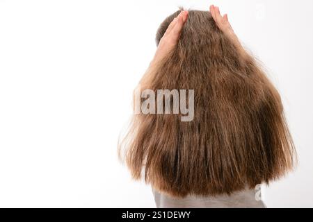 Eine Person mit sehr langem, hellbraunem Haar wird von hinten gesehen, die Hände liegen leicht auf dem Kopf. Das Haar erscheint gesund und ist der wichtigste foc Stockfoto