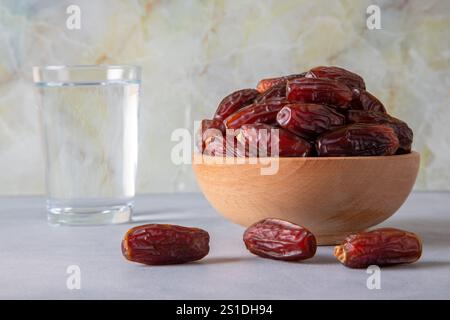 Datteln Obst in einer Holzschale und ein Glas Wasser daneben. Das Fastenbrechen mit Dates ist eine Tradition für Muslime. Stockfoto
