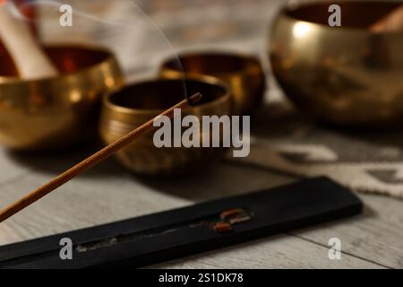 Räucherstäbchen schwelend im Halter und tibetische Klangschalen auf dem Boden, Nahaufnahme Stockfoto