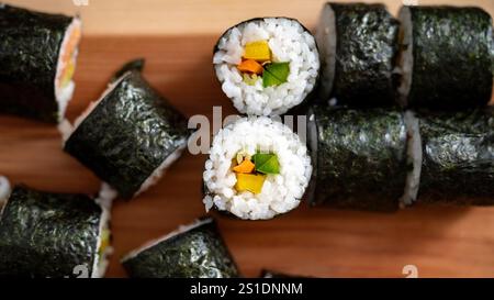Eine Nahaufnahme frisch zubereiteter Sushi-Brötchen, gefüllt mit bunten Gemüse, ordentlich auf einer Holzoberfläche angeordnet. Stockfoto