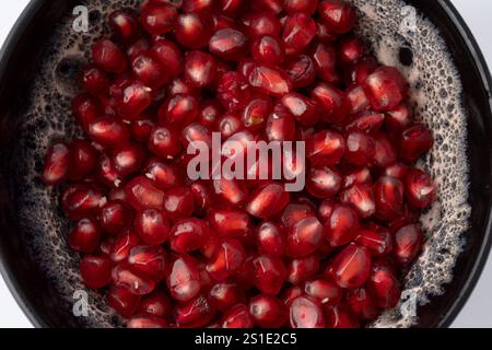 Nahaufnahme einer grauen und weißen Tonschale, gefüllt mit roten dreieckigen Granatapfelkernen auf weißem Hintergrund Stockfoto