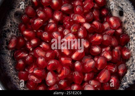 Nahaufnahme einer grauen und weißen Tonschale, gefüllt mit roten dreieckigen Granatapfelkernen auf weißem Hintergrund Stockfoto