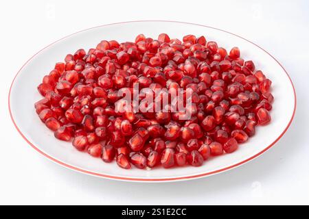 Nahaufnahme einer weißen Platte, gefüllt mit roten dreieckigen Granatapfelkernen auf weißem Hintergrund Stockfoto