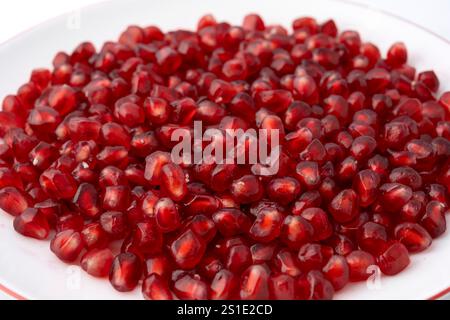 Nahaufnahme einer weißen Platte, gefüllt mit roten dreieckigen Granatapfelkernen auf weißem Hintergrund Stockfoto