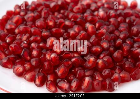Nahaufnahme einer weißen Platte, gefüllt mit roten dreieckigen Granatapfelkernen auf weißem Hintergrund Stockfoto