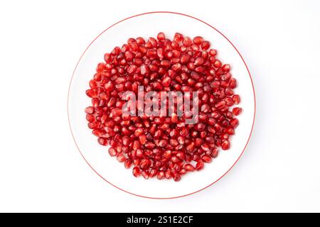 Nahaufnahme einer weißen Platte, gefüllt mit roten dreieckigen Granatapfelkernen auf weißem Hintergrund Stockfoto