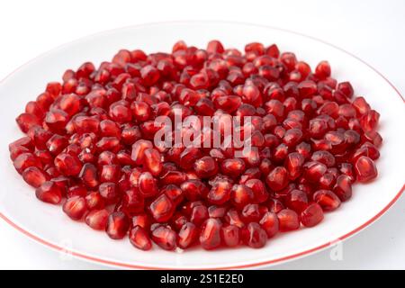 Nahaufnahme einer weißen Platte, gefüllt mit roten dreieckigen Granatapfelkernen auf weißem Hintergrund Stockfoto