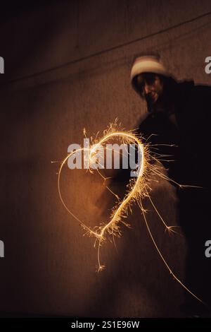 Mädchen, das Herz mit Gefrierlicht malt. Herzform mit festlichen, eiskalten Lichtern in der Nacht. Funkelndes Herz aus Feuer. Zeichnungen für Bremslicht. Stockfoto