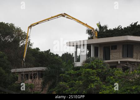 Bautätigkeit mit einer Betonpumpe, die sich über ein neues Gebäude in tropischer Umgebung erstreckt. Stockfoto