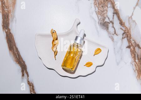 Eine durchsichtige Flasche mit einem natürlichen Kosmetikprodukt für die Gesichtspflege Panthenol, Gold 24k auf Tablett in Form einer Schale. Abstrakter Marmor. Draufsicht Stockfoto