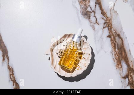 Naturkosmetikum zur Gesichtshaut-Pflege, Serum in einer Glasflasche mit Tropfer auf einem Tablett in Form einer Schale. Gold 24k. Pflege der Haut. Stockfoto