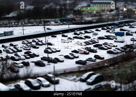 Ein riesiger Parkplatz mit vielen Autos auf einer Winterstraße. Schneebedeckte Stadtstraße aus der Vogelperspektive Tilt Shift-Effekt. Kalte Jahreszeit Wetter im Freien. Stockfoto