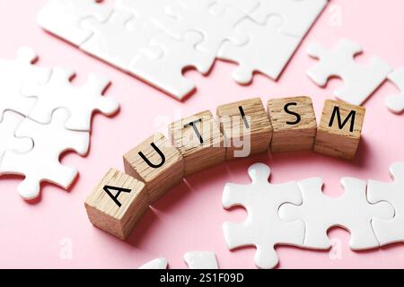 Wort Autismus gemacht mit Holzwürfeln und Puzzleteilen auf rosa Hintergrund, Nahaufnahme Stockfoto