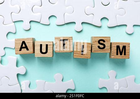 Wort Autismus gemacht mit Holzwürfeln und Puzzleteilen auf hellblauem Hintergrund, flache Lay Stockfoto