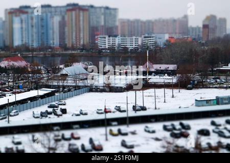 Ein riesiger Parkplatz mit vielen Autos auf einer Winterstraße. Schneebedeckte Stadtstraße aus der Vogelperspektive Tilt Shift-Effekt. Kalte Jahreszeit Wetter im Freien. Stockfoto