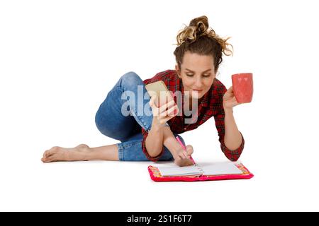 Die junge süße Frau macht Notizen in Notizbuch, trinkt Kaffee und spricht auf einem Handy in einer Yoga-Pose isoliert auf weißem Hintergrund Stockfoto