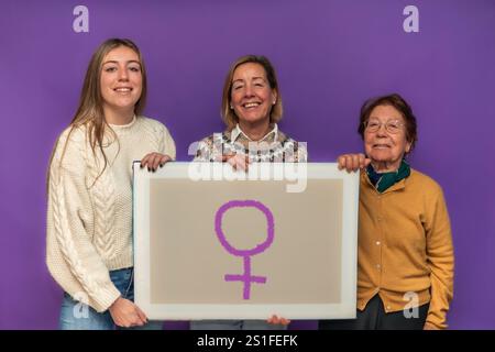Drei Generationen von Frauen lächeln, während sie eine Leinwand mit dem weiblichen Geschlechtersymbol halten, um den Frauentag und den Feminismus vor einem lebhaften P zu feiern Stockfoto