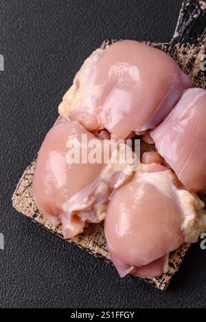 Frische rohe Hähnchenschenkel-Filets mit Salz, Gewürzen und Kräutern auf dunklem Betonhintergrund Stockfoto