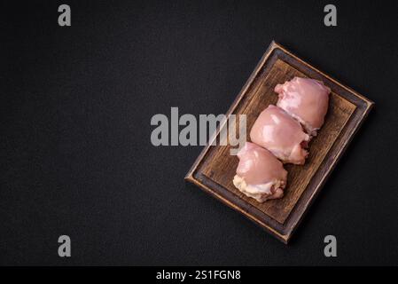 Frische rohe Hähnchenschenkel-Filets mit Salz, Gewürzen und Kräutern auf dunklem Betonhintergrund Stockfoto