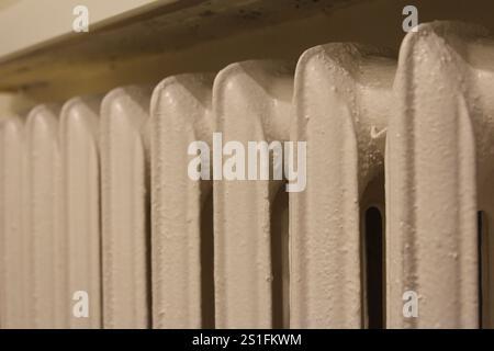 Nahaufnahme eines weißen Heizkörpers, der Kondenswasser auf seiner Oberfläche zeigt und sich in einer warmen Innenumgebung befindet. Stockfoto