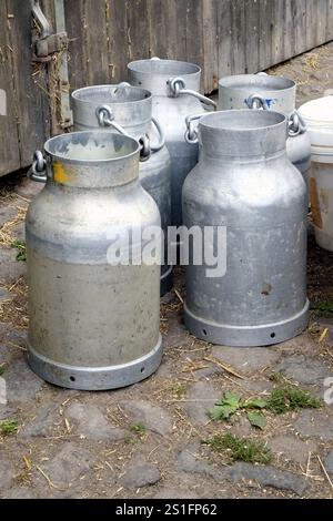 Große silberne Milchkannen aus Metall vor der Scheunentür einer Farm. Hochformat. Große silberne Metallmilch wirbelt vor der Scheunentür eines Bauernhofs. Stockfoto