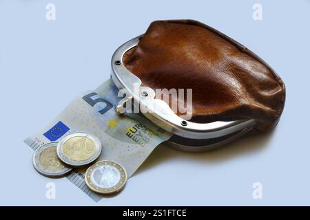 Leicht geöffnete, altmodische Geldbörse aus braunem Leder mit herausragender Banknote und drei Euro-Münzen davor. Ausschnitt. Querformat f Stockfoto