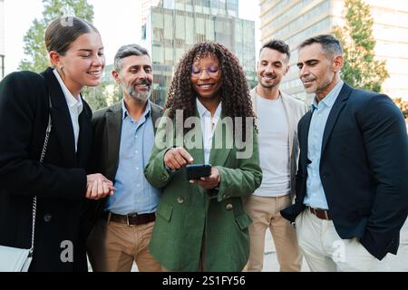 Gruppe verschiedener Kollegen, die im Außenbereich ein Smartphone anschauen, diskutierten. Teamarbeit von multirassischen Geschäftsleuten, Zusammenarbeit und Technologie im beruflichen Kontext. Hochwertige Fotos Stockfoto