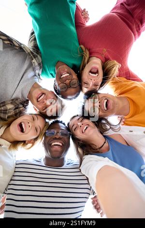 Selfie von unten mit verschiedenen Gruppenfreunden, die sich im Kreis umarmen und begeistert in die Kamera schauen Stockfoto