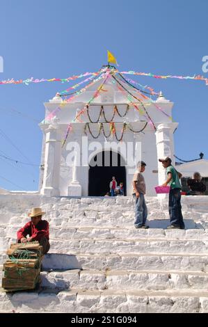 Kirche Capilla del Calvario Chichicastenango Guatemala / CHICHICASTENANGO, Guatemala - Ein Mann, der Brennholz verkauft, liegt auf den Stufen der Capilla del Calvario, einer weiß getünchten Kirche im Zentrum von Chichicastenango, direkt gegenüber der Kirche Santo Tomas. Chichicastenango ist eine indigene Maya-Stadt im guatemaltekischen Hochland etwa 90 Meilen (145 km) nordwestlich von Guatemala-Stadt auf einer Höhe von fast 6.500 Fuß (1.980 Meter). Die Stadt ist bekannt für ihre lebhaften Märkte, die donnerstags und sonntags stattfinden und sowohl Einheimische als auch Touristen auf der Suche nach traditionellen Maya-Textilien, Kunsthandwerk, Stockfoto