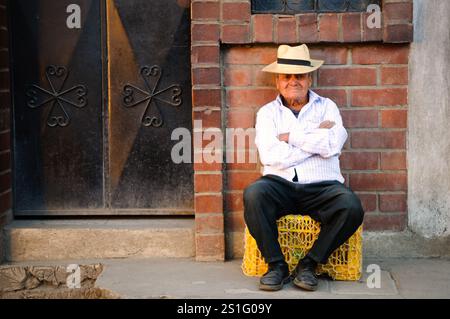 Maya Man Portrait Chichicastenango Guatemala | CHICHICASTENANGO, Guatemala — Ein Mann sitzt für ein Porträt auf einer Straße in Chichicastenango, einer indigenen Maya-Stadt im Hochland von Guatemala. Chichicastenango (auch bekannt als Santo Tomás Chichicastenango) liegt etwa 90 Meilen (145 Kilometer) nordwestlich von Guatemala-Stadt auf einer Höhe von fast 6.500 Fuß (1.980 Meter). Die Stadt ist berühmt für ihre farbenfrohen Märkte, die an Donnersdagen und Sonntagen stattfinden und sowohl Einheimische als auch Touristen anziehen, die traditionelle Maya-Textilien, Handwerksprodukte und landwirtschaftliche Erzeugnisse suchen. Stockfoto
