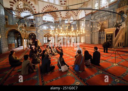 Rustem Pascha Moschee Innen Iznik Fliesen Istanbul // ISTANBUL, Türkei - Eine Gruppe von Touristen sitzt auf dem roten Teppichboden des Gebetssaals und hört ihrem Reiseleiter unter der großen Mahhya zu. Die zentrale Kuppel der Rustem-Pascha-Moschee (auch bekannt als Rüstem Paşa Camii) zeigt eine komplexe Kombination aus Iznik-Fliesen und bemalter Dekoration, die ein Beispiel für das klassische osmanische Design darstellt. Die 1563 vom Architekten Mimar Sinan erbaute Kuppel erhebt sich 15 Meter (49 Fuß) im Durchmesser über dem Gebetssaal. Die Moschee besteht aus etwa 2.300 einzelnen Iznik-Fliesen, die in etwa 80 verschiedenen Mustern angeordnet sind Stockfoto