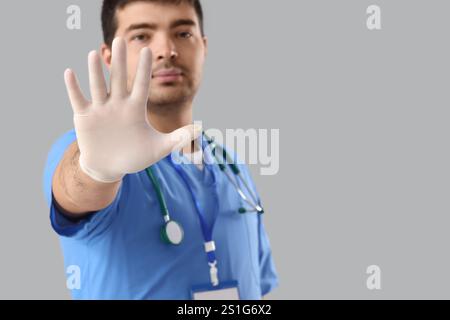 Männlicher Arzt zeigt STOP-Geste auf grauem Hintergrund Stockfoto