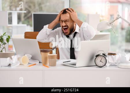 Ein gestresster Geschäftsmann, der im Büro einen Tisch anschreit Stockfoto